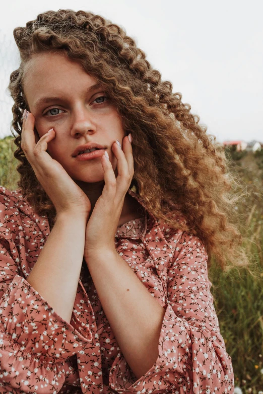 a woman sitting in a field with her hands on her face, by Sara Saftleven, trending on pexels, renaissance, curly middle part haircut, portrait sophie mudd, teenager, curly blonde hair | d & d