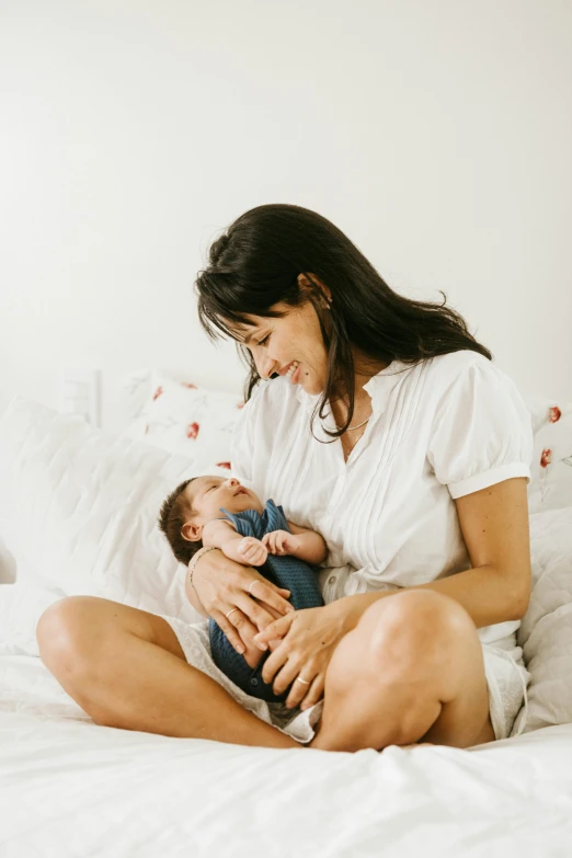 a woman sitting on a bed holding a baby, pexels contest winner, jen atkin, holding a milkor mgl, open belly, very calm and wholesome