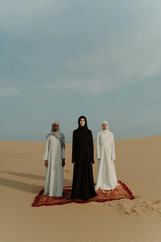 a group of people standing on top of a desert, an album cover, trending on unsplash, hurufiyya, wearing simple robes, three women, ( ( theatrical ) ), veiled