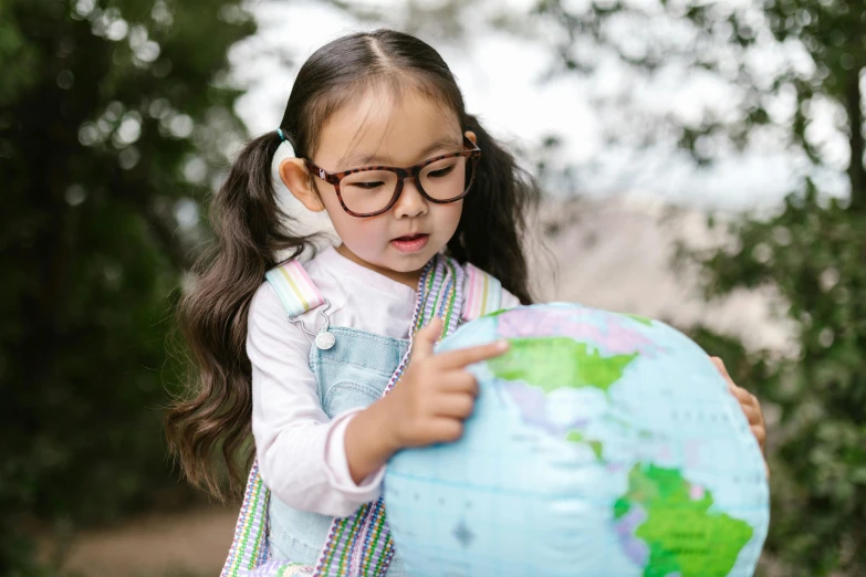 a little girl holding a globe in her hands, pexels contest winner, square rimmed glasses, asian female, looking across the shoulder, world map