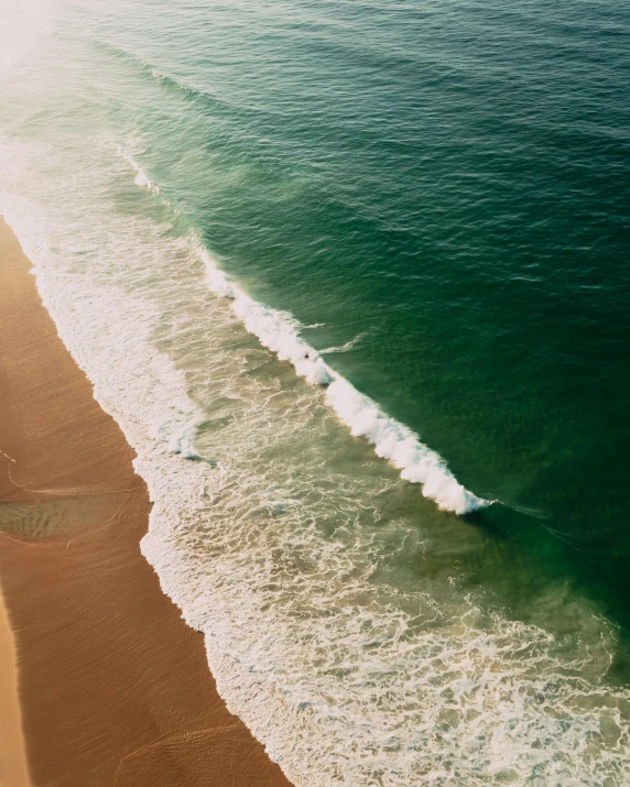 a person riding a surfboard on top of a sandy beach, dark green water, as far as the eye can see, arial shot, a photo of the ocean