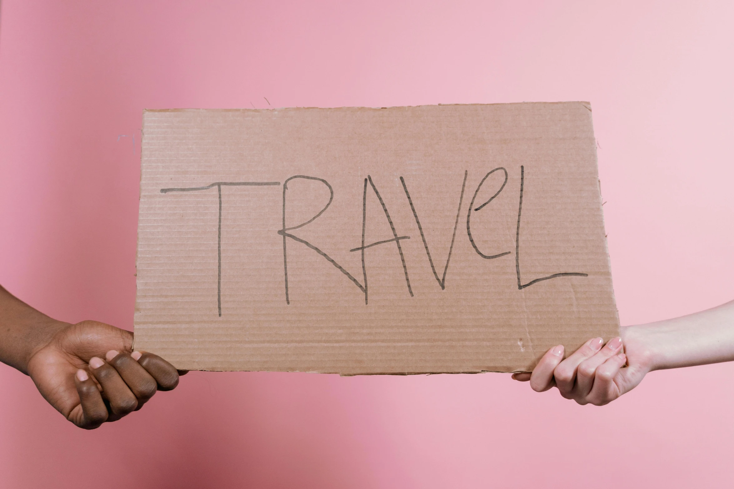 two people holding a cardboard sign that says travel, by Carla Wyzgala, pexels contest winner, ((pink)), one line, college, handheld