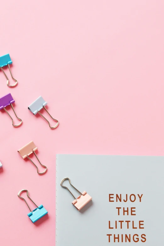 a pile of paper clips next to a piece of paper with the words enjoy the little things, trending on unsplash, pink pastel, knolling, promo image, zippers