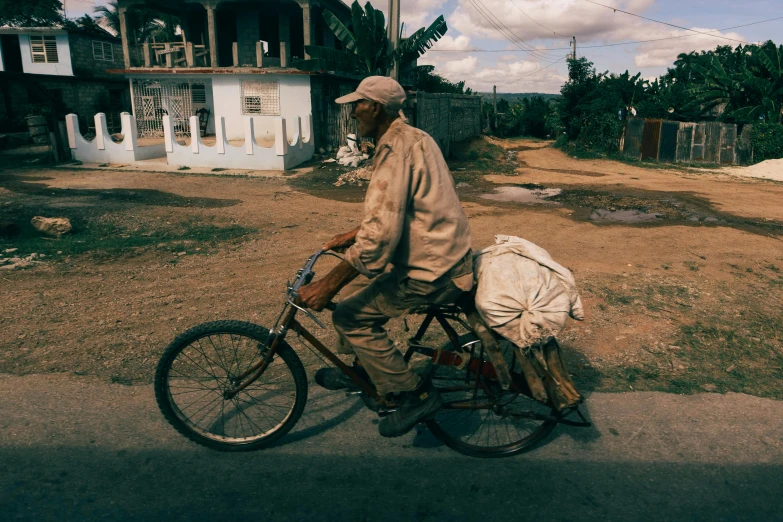 a man riding a bike with a bag on the back, by Will Ellis, pexels contest winner, photorealism, jamaica, old man, helio oiticica, dressed in a worn