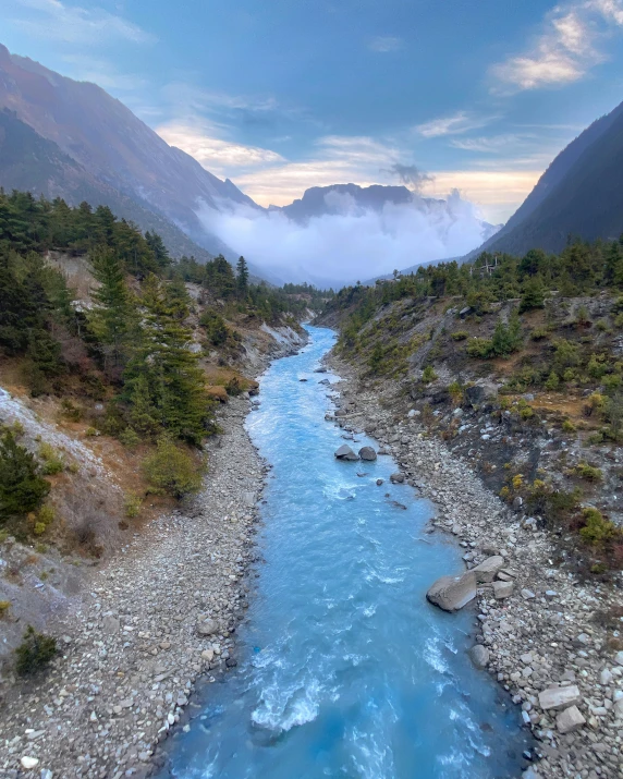 a river flowing through a lush green forest filled valley, by Daren Bader, pexels contest winner, hurufiyya, blue glacier, himalayas, blue and white and red mist, early evening