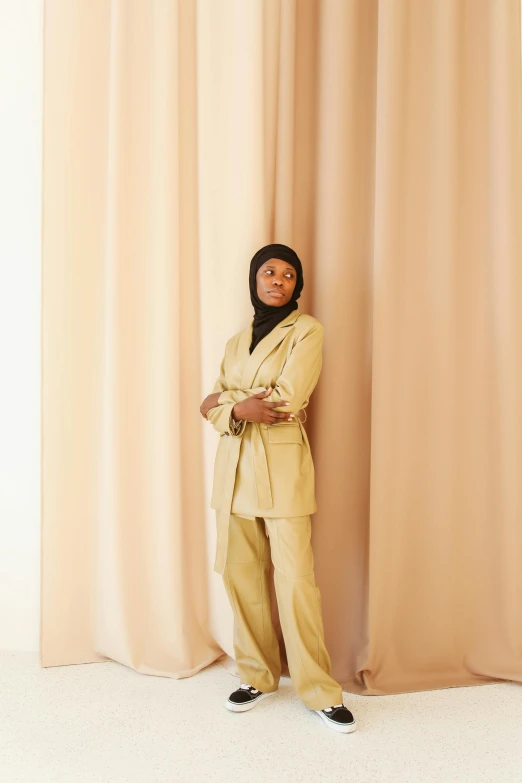 a woman standing in front of a curtain, an album cover, trending on pexels, hurufiyya, tan suit, riyahd cassiem, at a fashion shoot, slight yellow hue