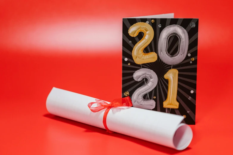 a graduation card sitting on top of a red table, by Julia Pishtar, pexels contest winner, new years eve, 1614572159, scrolls, 2 0 2 1