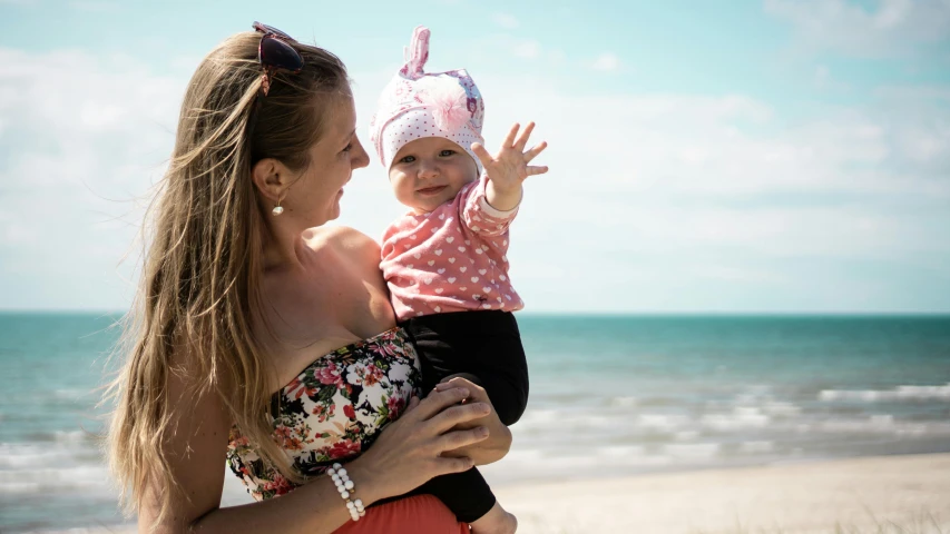 a woman holding a baby on the beach, a portrait, pixabay, square, portrait image, super high resolution, waving