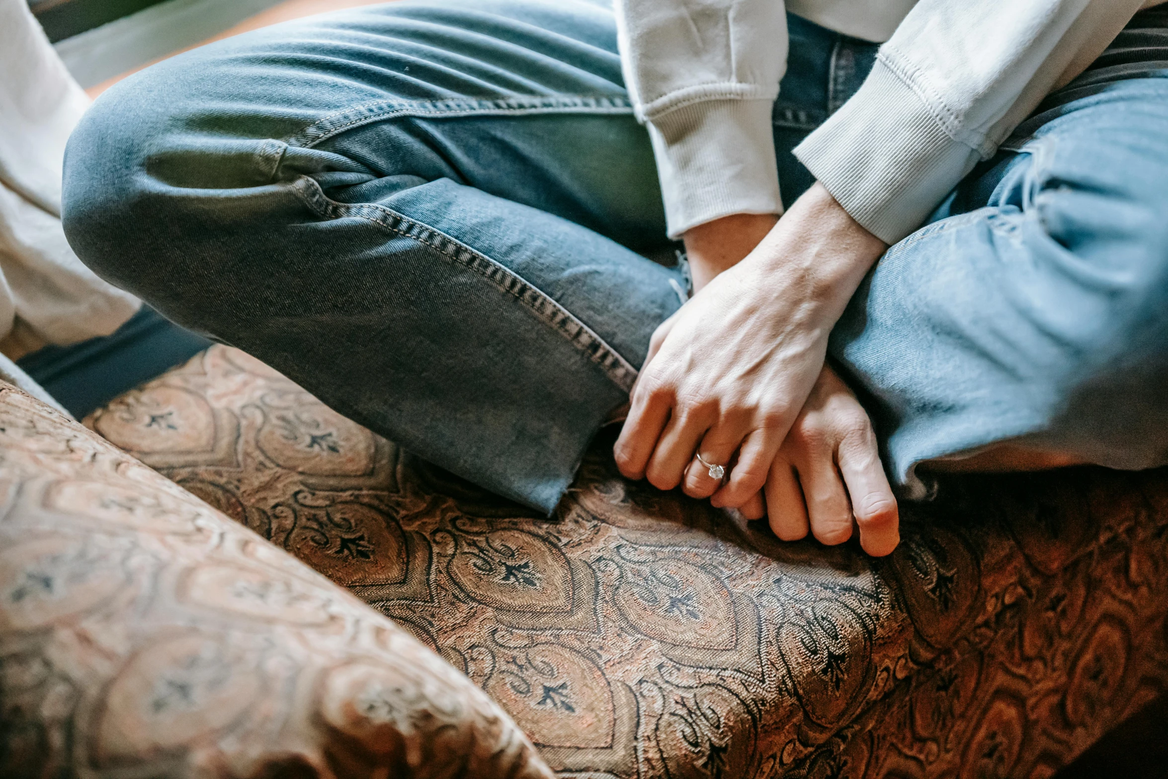 a close up of a person sitting on a couch, by Nina Hamnett, trending on pexels, holding each other hands, jeans, romantic lead, lightly dressed