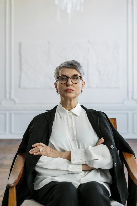 a woman sitting in a chair with her arms crossed, inspired by Ruth Deckard, trending on pexels, short grey hair, architect, androgynous male, maurizio cattelan