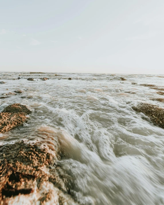 a man standing on top of a rock next to the ocean, an album cover, unsplash contest winner, ferrofluid oceans, river rapids, brown mud, covered in coral and barnacles