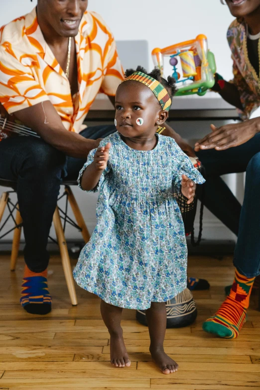 a group of people sitting on top of a wooden floor, an album cover, by Ingrida Kadaka, pexels contest winner, black arts movement, toddler, wearing an african dress, multicoloured, walking down