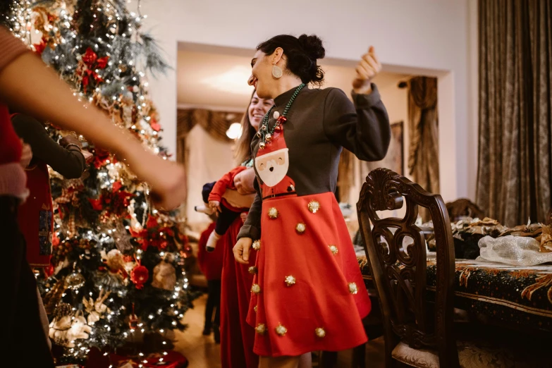 a woman standing in front of a christmas tree, pexels contest winner, happening, other women dancing behind, wearing a fancy dress, avatar image, joyful people in the house