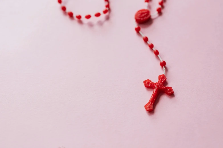 a close up of a rosary on a pink surface, pexels, plasticien, wearing red attire, 3 d print, crosses, instagram post