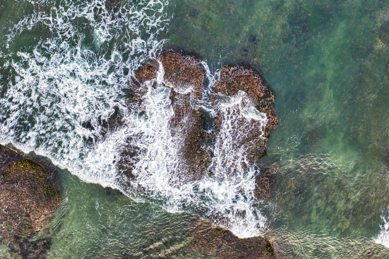 a bird's eye view of a body of water, by Peter Churcher, pexels contest winner, hurufiyya, waves crashing at rocks, forming a heart with their necks, manly, slightly pixelated