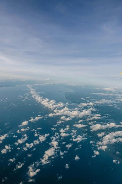 the wing of an airplane flying over the ocean, by Peter Churcher, unsplash, hot air balloons, “puffy cloudscape, yellow, mariana trench