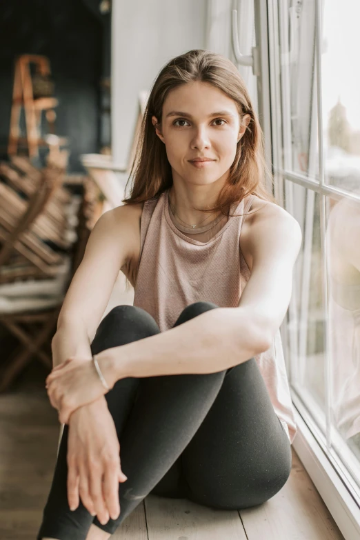 a woman sitting on the floor in front of a window, a portrait, by Grace Polit, trending on unsplash, wearing a muscle tee shirt, erin moriarty, girl with brown hair, half - length photo