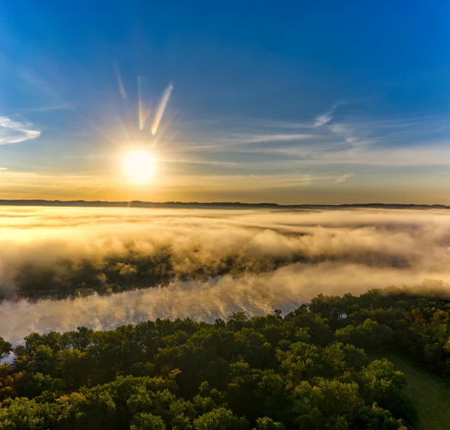 a large body of water surrounded by trees, by Matt Cavotta, pexels contest winner, hudson river school, above low layered clouds, sun rising, drone photograpghy, panoramic shot