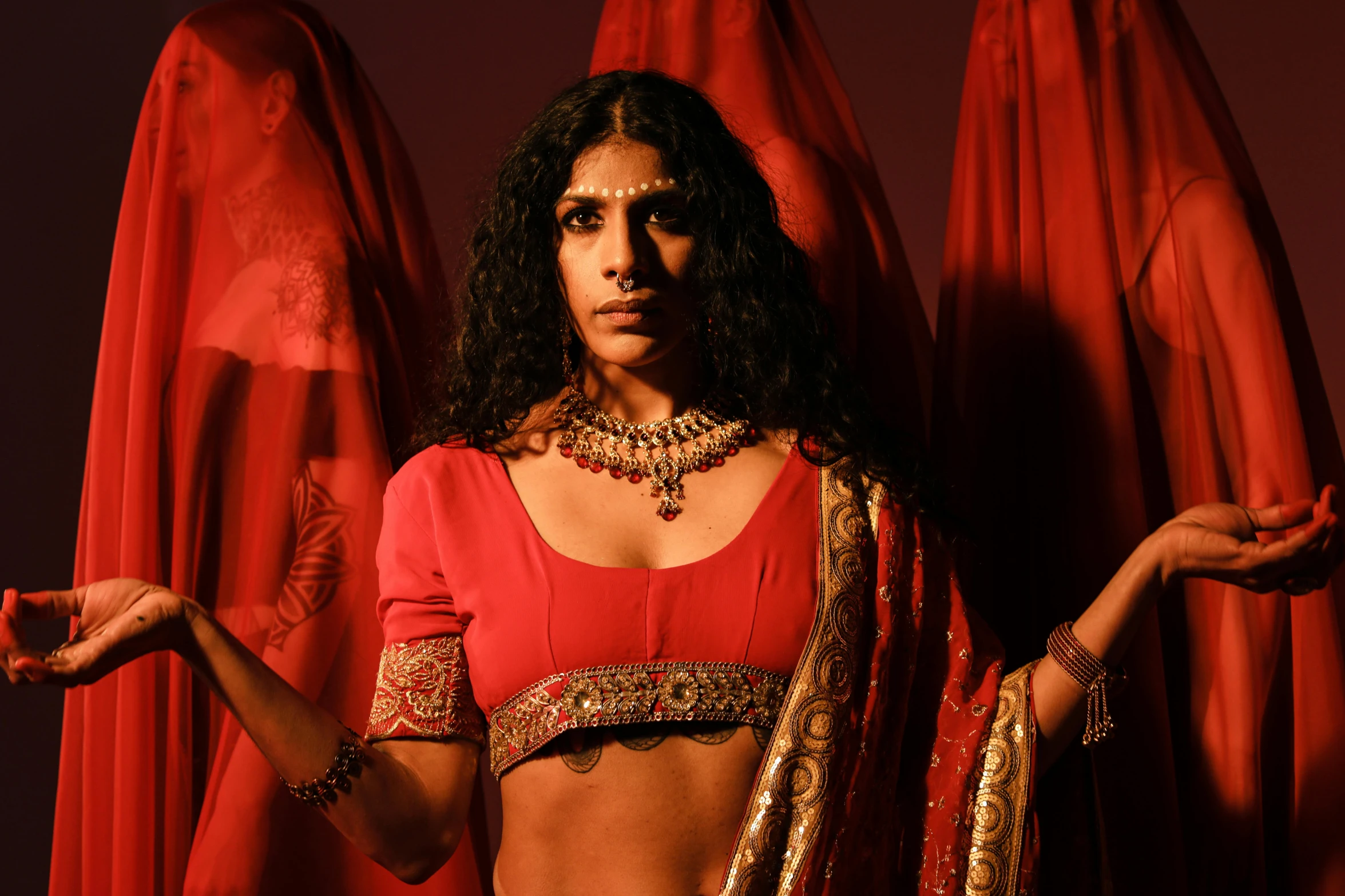 a woman in a red outfit holding her hands out, an album cover, inspired by Raja Ravi Varma, transgressive art, trans rights, in a movie still cinematic, [ theatrical ], drag