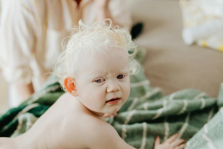 a baby sitting on top of a bed next to a woman, by Emma Andijewska, trending on pexels, albino hair, wearing a towel, closeup face, dressed in a green robe