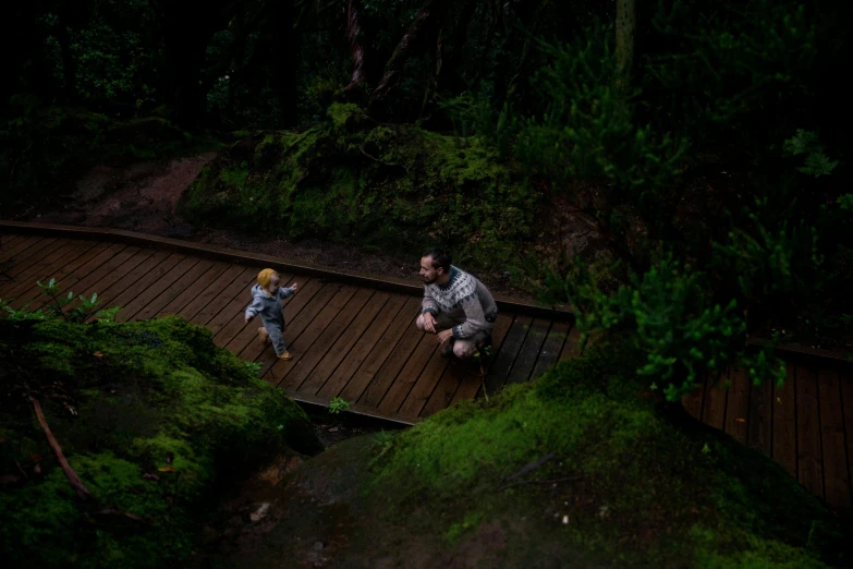 a man and a child sitting on a wooden bridge in the woods, a picture, by Elsa Bleda, pexels contest winner, crawling along a bed of moss, avatar image, fisher price redwood forest, (night)