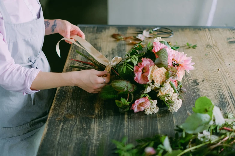 a woman cutting flowers with a pair of scissors, a still life, unsplash, back towards camera, on wooden table, looking left, where a large