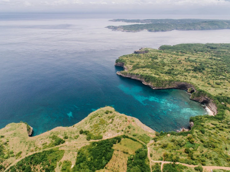 a large body of water next to a lush green hillside, by Simon Marmion, pexels contest winner, coral reefs, bali, aerial footage, coastal cliffs