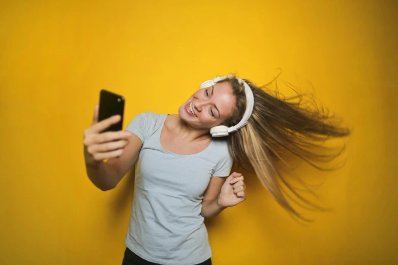 a woman with headphones listening to music on her phone, pexels, happening, wavy hair yellow theme, taking a selfie, dancing, a single