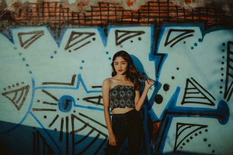 a woman standing in front of a graffiti covered wall, an album cover, inspired by Elsa Bleda, trending on pexels, graffiti, croptop, beautiful young asian woman, black and blue, 2 4 year old female model