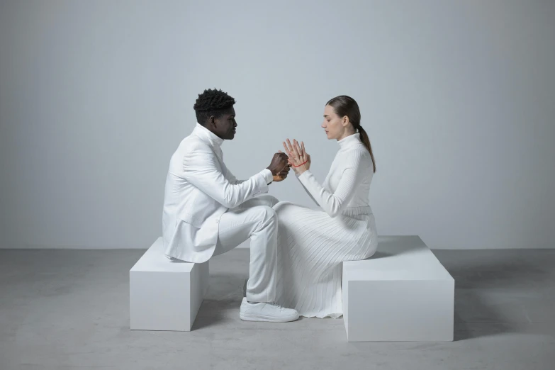 a man and a woman sitting on a white bench, an album cover, wearing futuristic white suit, blessing hands, voxelart, riyahd cassiem