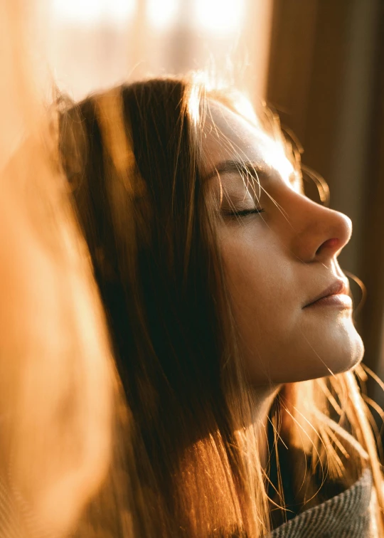 a woman sitting in front of a window with her eyes closed, trending on pexels, sunny amber morning light, close up of face, young woman looking up, protruding chin