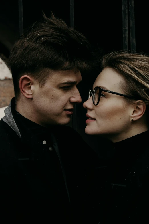 a man and a woman standing next to each other, trending on pexels, wearing black frame glasses, russian girlfriend, intimate dark moody, thick jawline