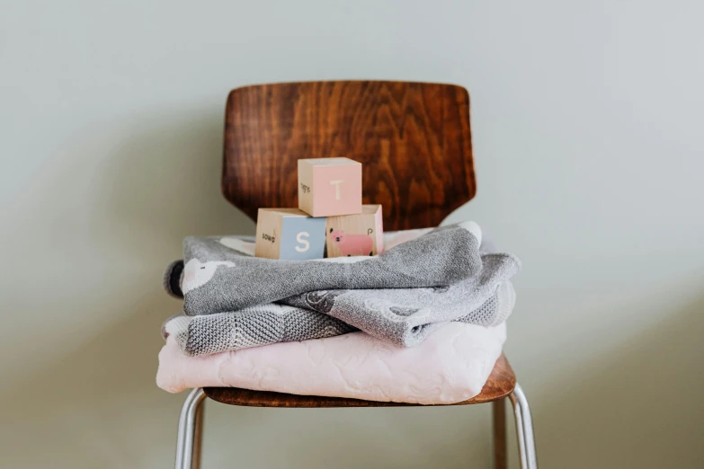 a stack of blankets sitting on top of a wooden chair, by Alice Mason, trending on unsplash, private press, cubes on table, pink pastel, miniature product photo, grey clothes