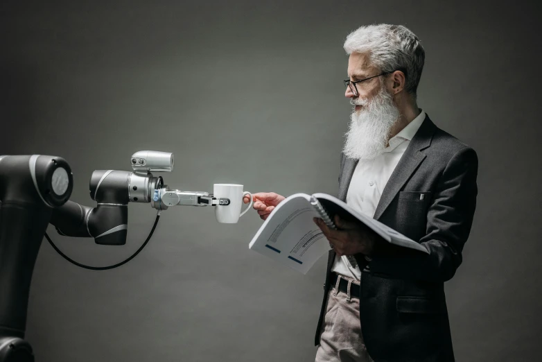 a man standing next to a robot holding a piece of paper, by Paul Bird, unsplash contest winner, very long silver beard, reading engineering book, looking to the side off camera, press shot