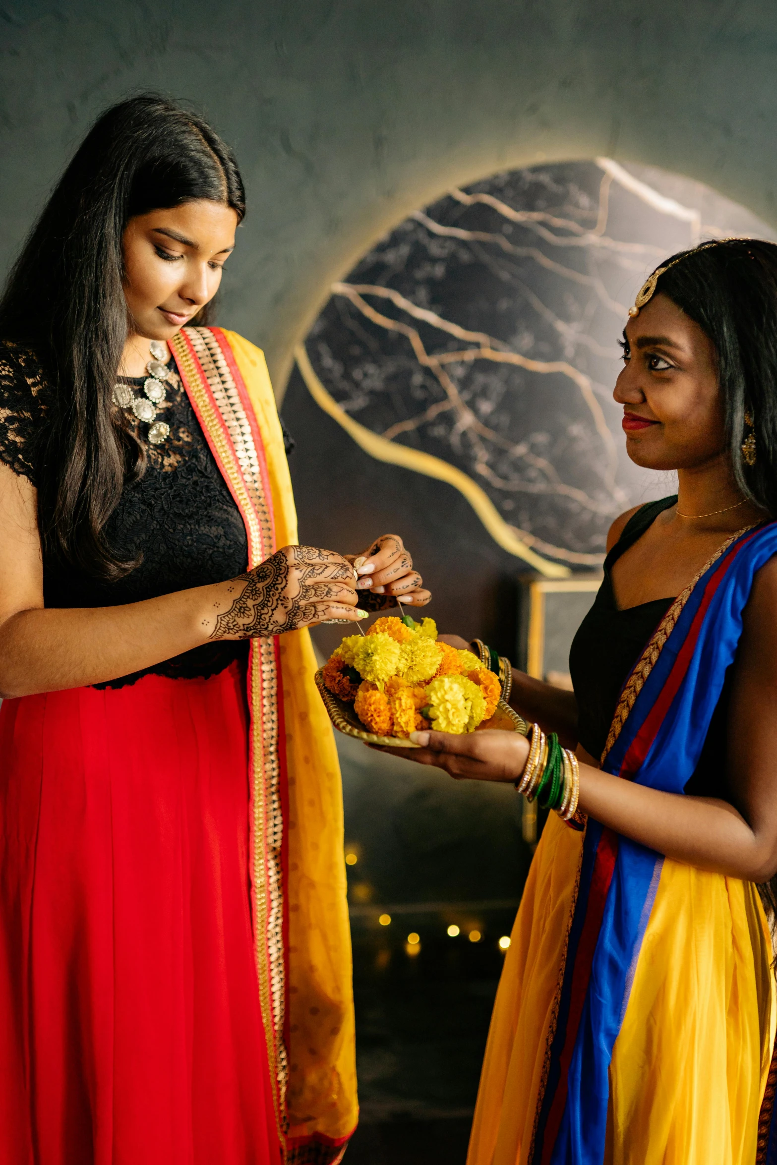 a couple of women standing next to each other, colorful adornments, offering a plate of food, hindu aesthetic, scarlet and yellow scheme