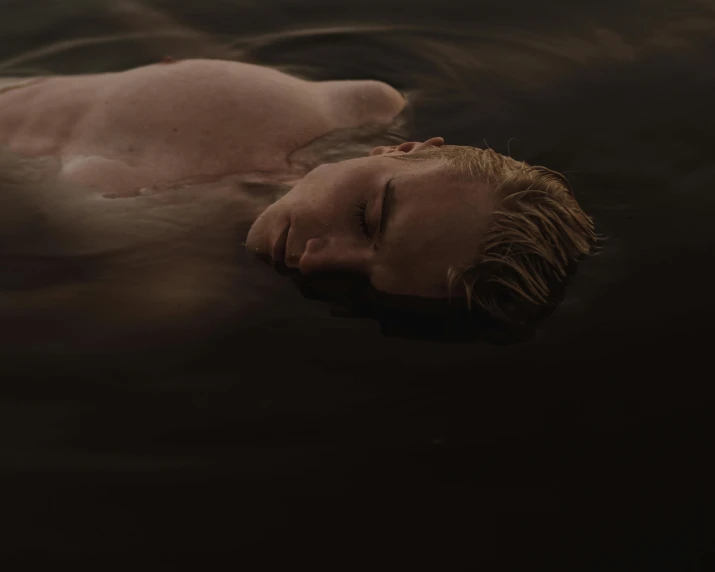 a man laying on top of a body of water, inspired by Elsa Bleda, pexels contest winner, massurrealism, pale skin curly blond hair, dark mood, carnal ) wet, low light cinematic