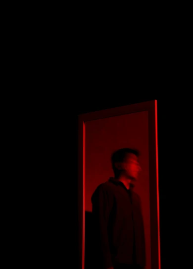 a man standing in front of a mirror in a dark room, an album cover, unsplash, conceptual art, red light, mingchen shen, ignant, black and red