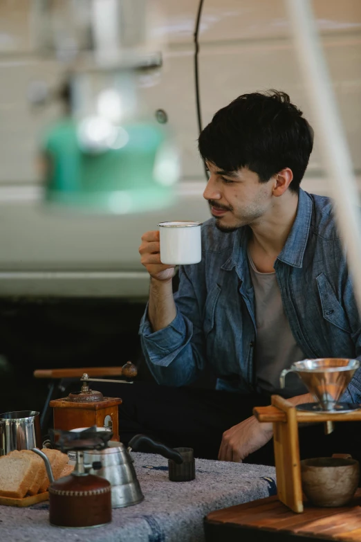 a man sitting at a table with a cup of coffee, trending in japan, mark edward fischbach, in a workshop, promo image