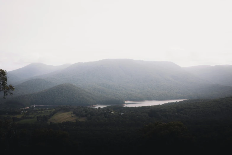 a large body of water sitting on top of a lush green hillside, by Morgan Russell, unsplash contest winner, australian tonalism, mountains and lakes, grey, concert, very hazy