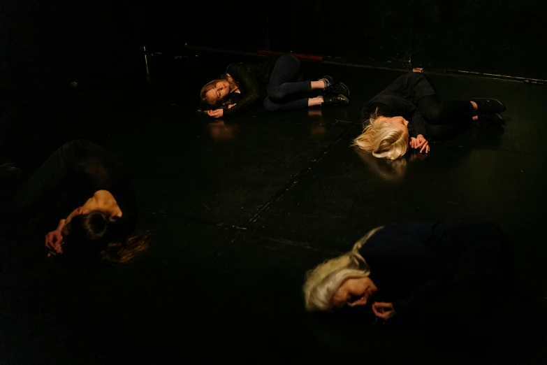 a group of people laying on the floor in a circle, by Helen Stevenson, in an empty black room, sirens, profile image, sweating