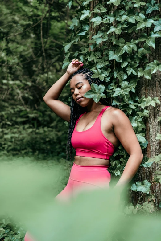 a woman leaning against a tree in the woods, by Dulah Marie Evans, pexels contest winner, two piece workout clothes, red tank-top, with ivy, african american young woman