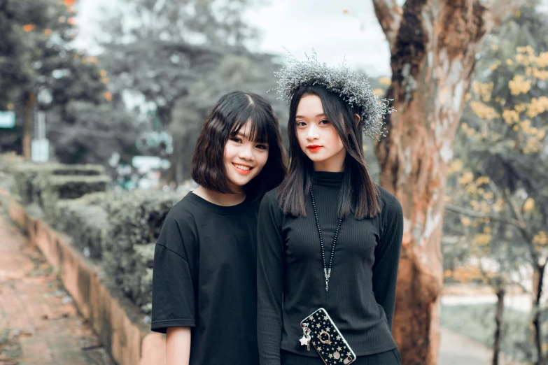 two women standing next to each other near a tree, by Tan Ting-pho, pexels contest winner, realism, wearing black stylish clothing, center parted bangs, beautiful young korean woman, wearing gothic accessories
