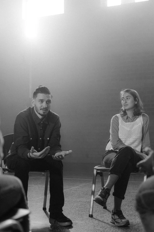 a group of people sitting in chairs in a room, a black and white photo, antipodeans, facing each other, pablo carpio and jordan grimmer, lena oxton, [ theatrical ]