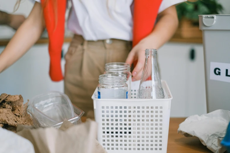 a woman standing next to a white basket filled with bottles, pexels contest winner, glass jar, recycled, white apron, filling with water