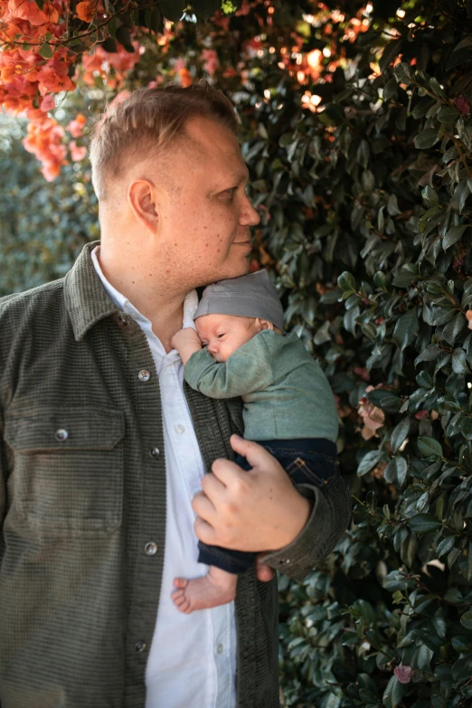 a man holding a baby in his arms, by Carey Morris, unsplash, vine covered, peter paul rebens, two handsome men, multi-part