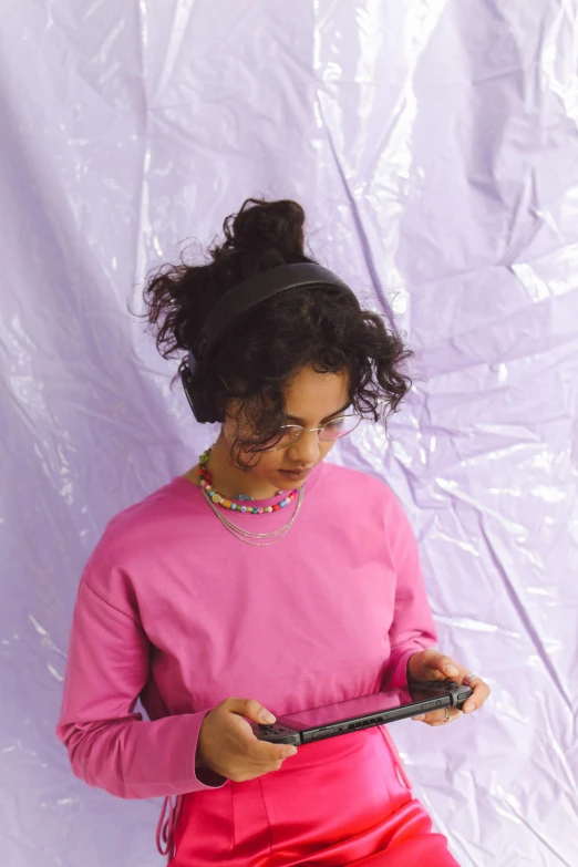 a woman in a pink shirt holding a cell phone, an album cover, computer art, wearing purple headphones, young middle eastern woman, loosely cropped, using a magical tablet