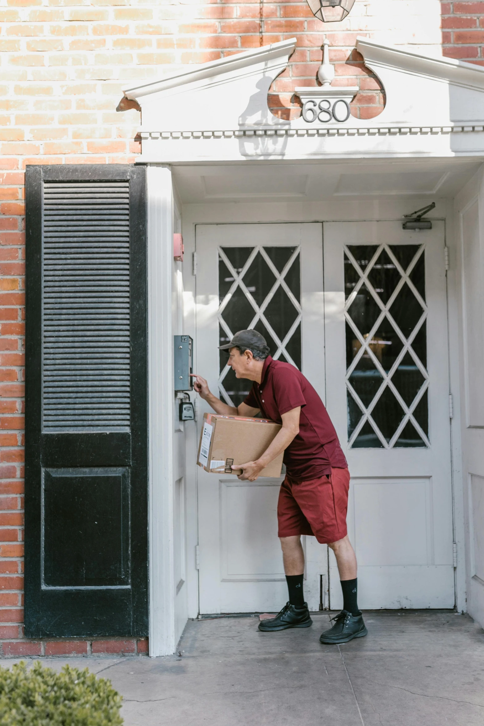 a man holding a box in front of a door, maroon and white, boston, pick wu, porches