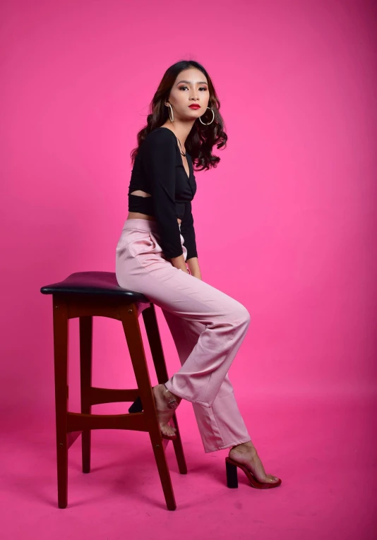 a woman sitting on top of a wooden stool, an album cover, by Basuki Abdullah, instagram, ((pink)), pants, elegant confident pose, pokimane