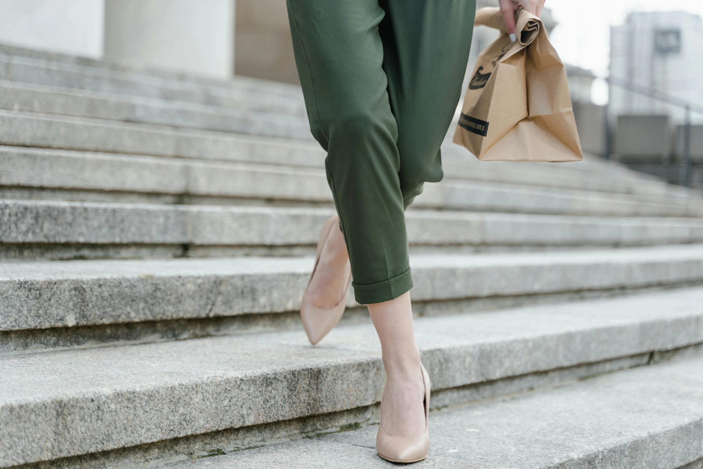 a woman walking up some steps carrying a bag, trending on pexels, olive green slacks, background image, wearing open toe heels, on high-quality paper