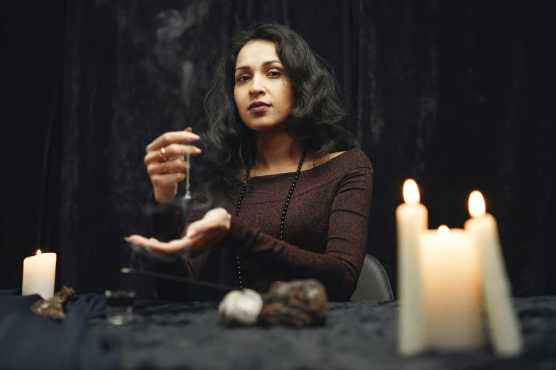 a woman sitting at a table with candles in front of her, trending on pexels, renaissance, wearing black wizard robes, black - haired mage, séance, a sorceress casting a ice ball